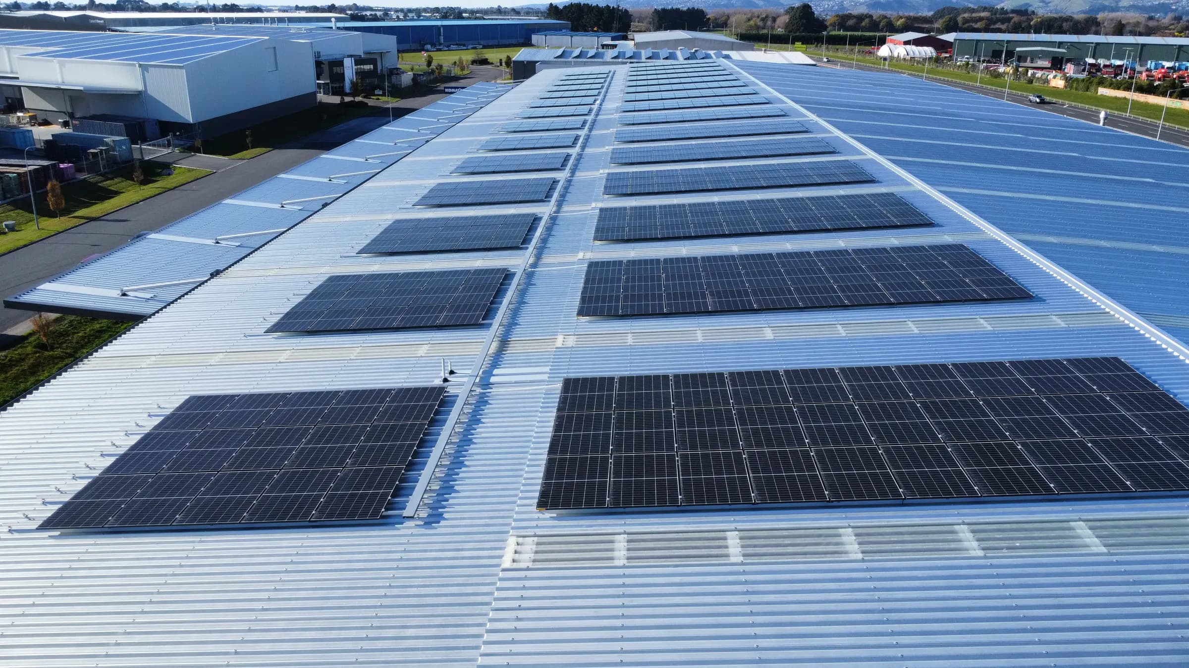 Low aerial view along rows of commercial solar panels on a warehouse roof